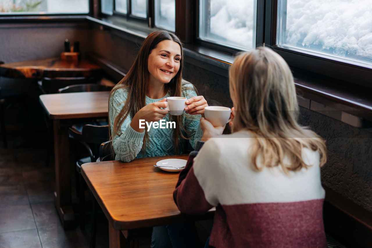 Smiling female brunette chatting with a female friend in a coffee shop.