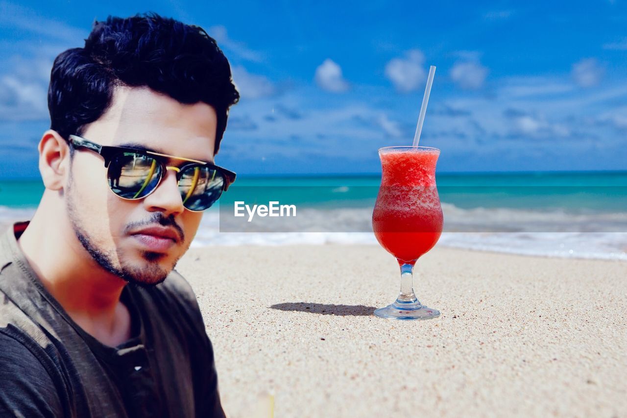 PORTRAIT OF YOUNG MAN WITH SUNGLASSES AT BEACH