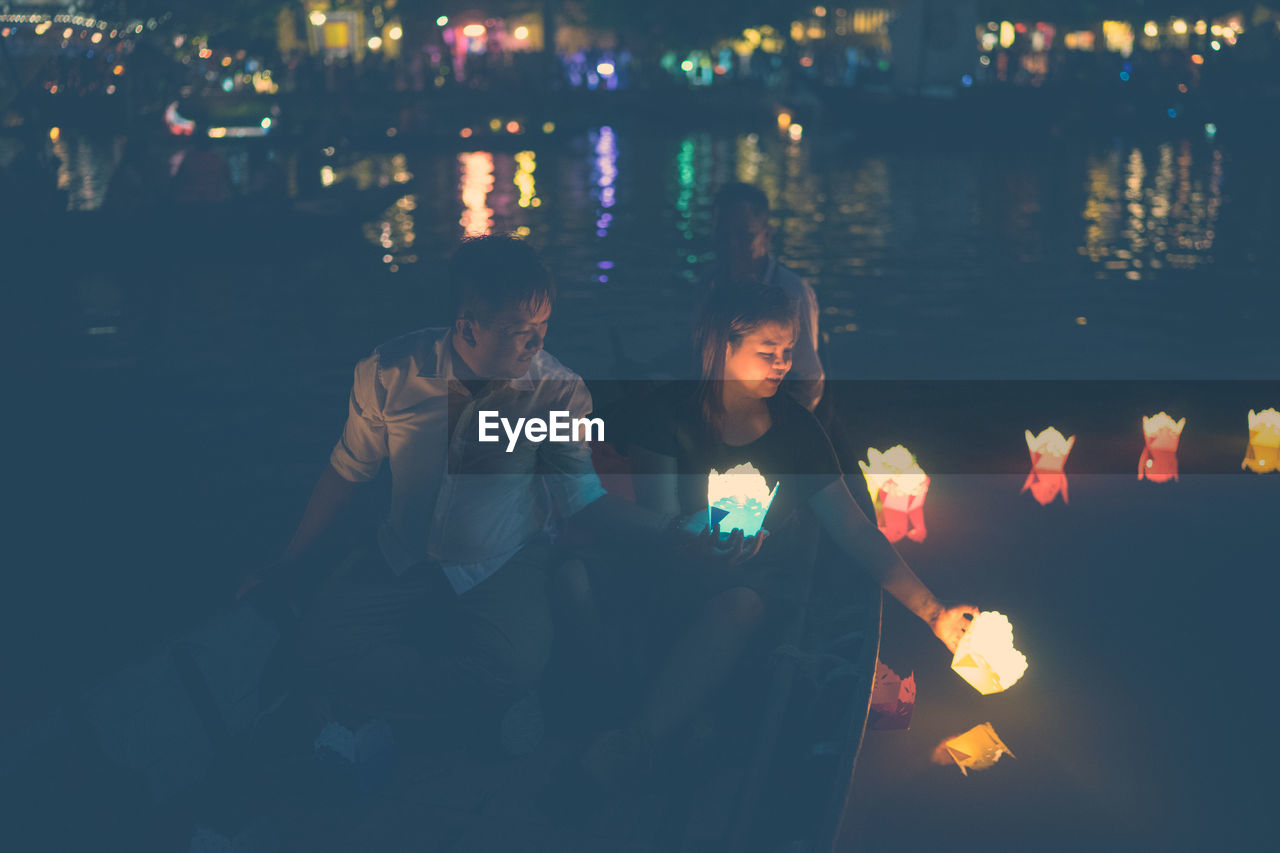 High angle view of people holding illuminated candles while sitting in boat on river at night