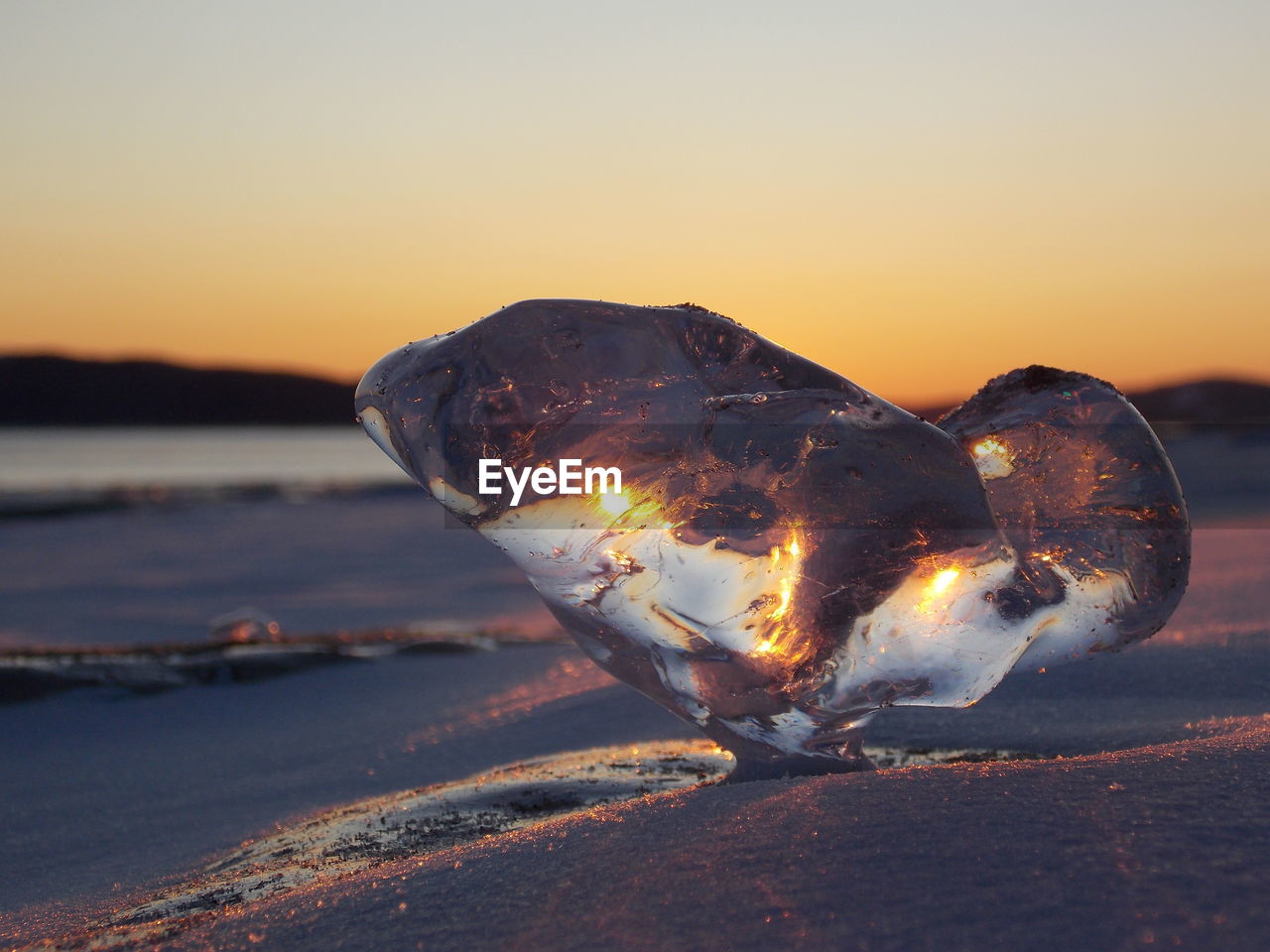 Close-up of icicles on beach against sky during sunset