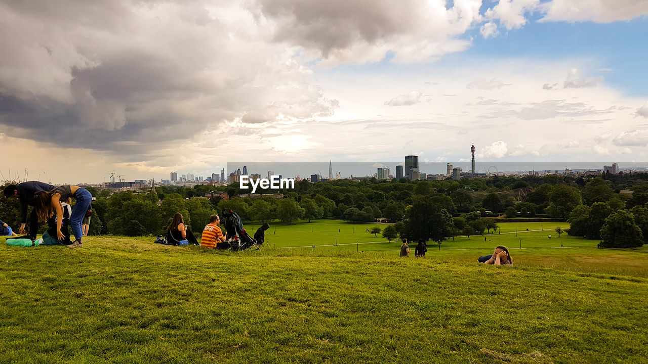 PEOPLE WALKING ON GRASSY FIELD AGAINST CLOUDY SKY