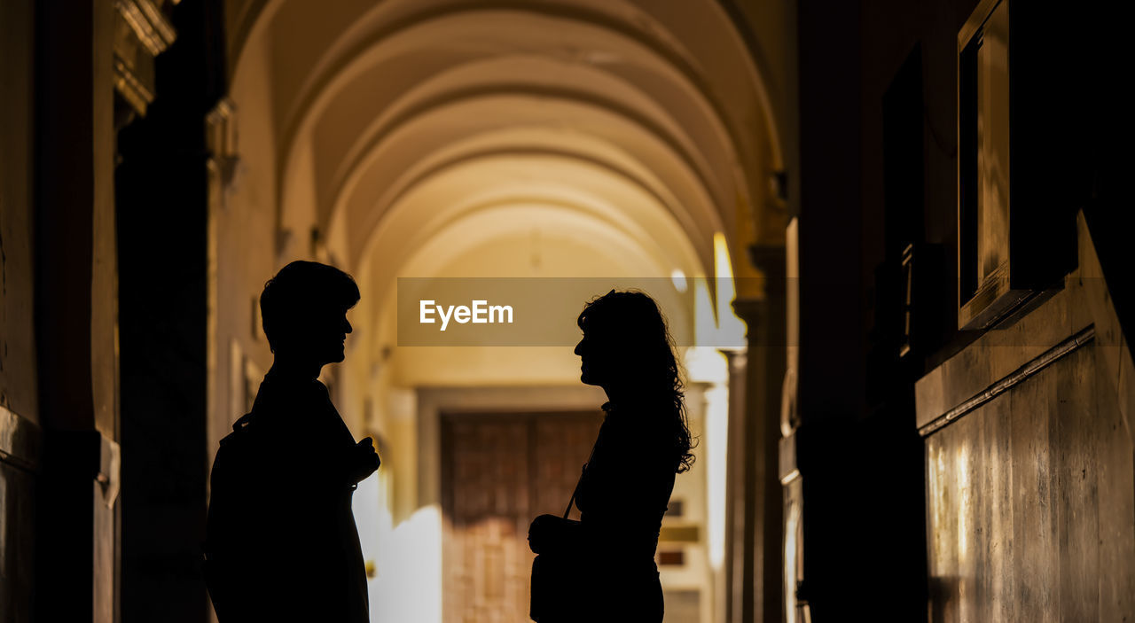 Silhouette of two young people chatting on building corridor with sunlight and shadow