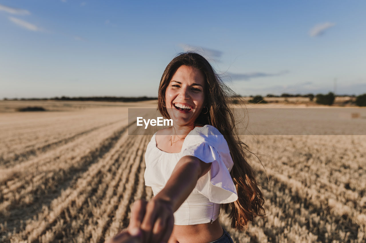 PORTRAIT OF SMILING YOUNG WOMAN ON FIELD