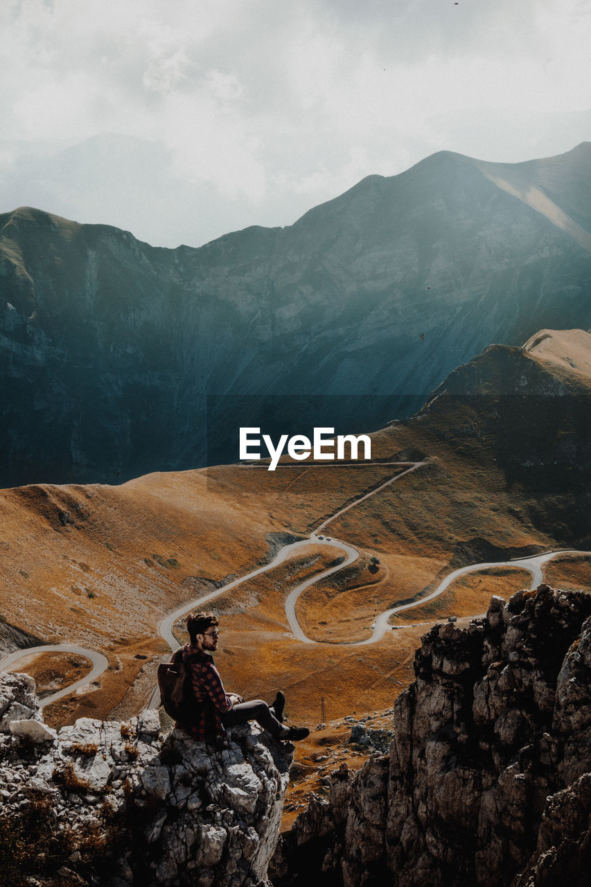 High angle view of man sitting on cliff against mountains