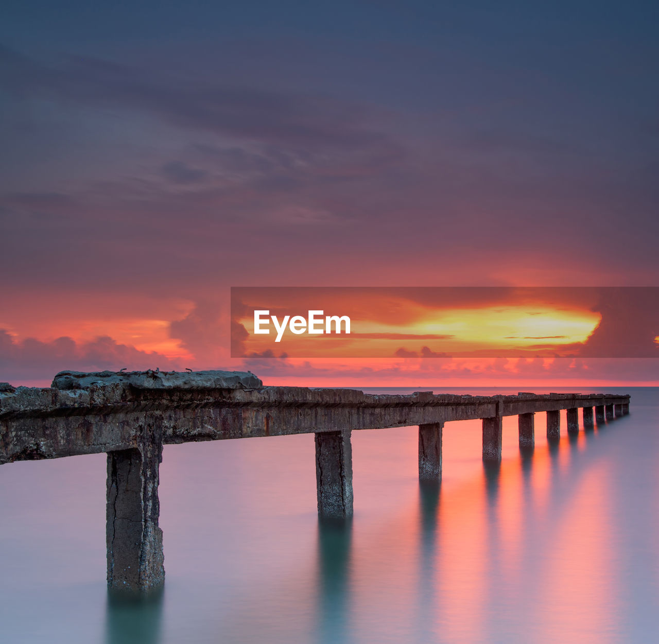 Abandoned pier over sea against cloudy sky during sunset