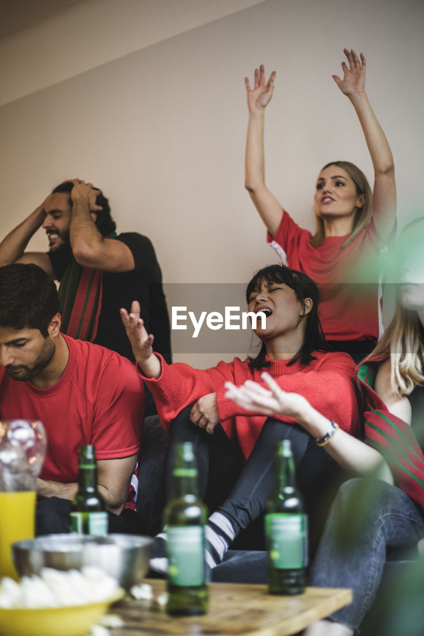 Sad male and female fans watching soccer match while sitting on sofa at home