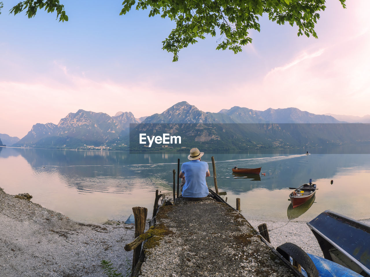 Italy, lombardy, back view of man sitting on jetty at lake idro at morning twilight