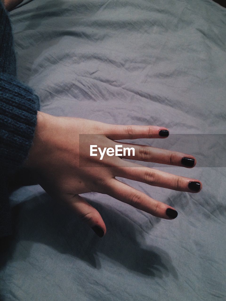 Cropped hand of woman showing black nail polish in bedroom