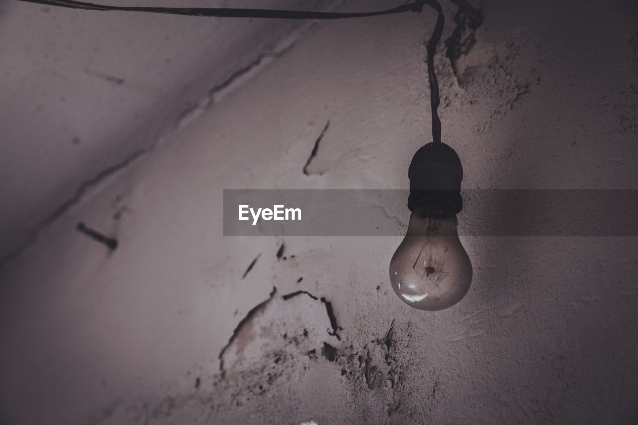 LOW ANGLE VIEW OF ILLUMINATED LIGHT BULB HANGING FROM WALL