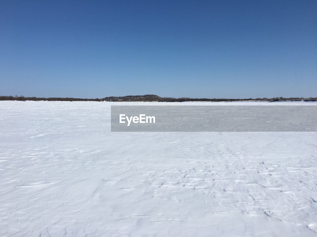 FROZEN LAKE AGAINST CLEAR BLUE SKY DURING WINTER