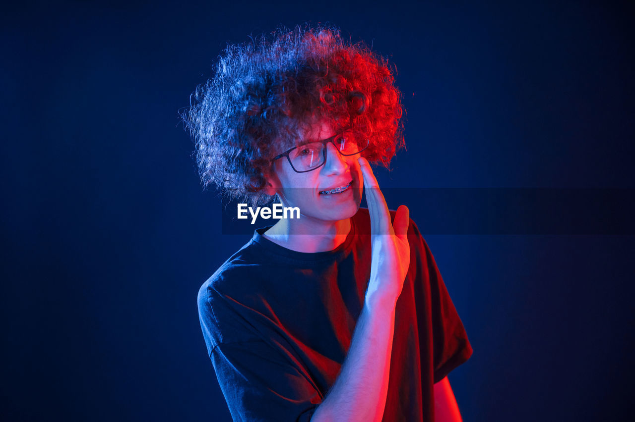 one person, studio shot, red, blue, redhead, young adult, portrait, indoors, performing arts, adult, hairstyle, dyed red hair, stage, human hair, entertainment, arts culture and entertainment, black background, curly hair, person, waist up, singing, colored background, performance, copy space, fashion, headshot, women, clothing