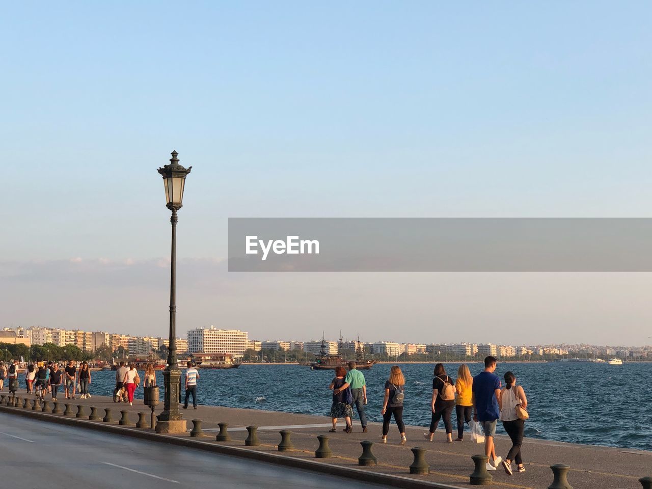 People on street by sea against clear sky