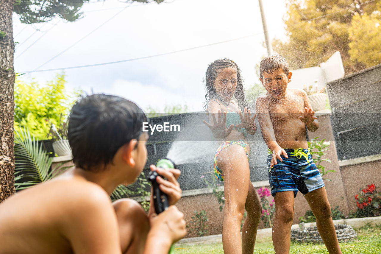 Three funny kids playing with a hose in the garden