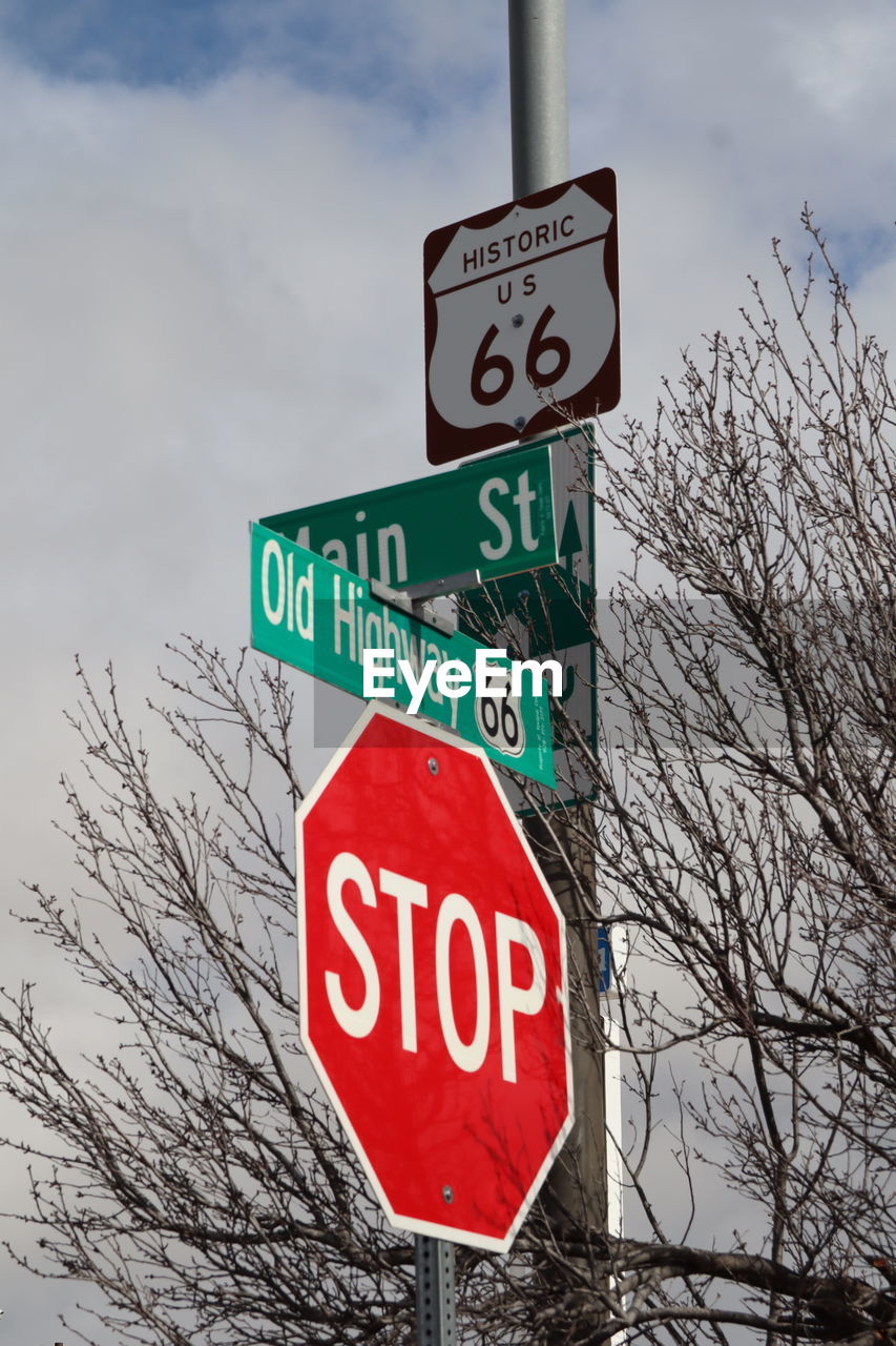 sign, communication, road sign, sky, text, tree, guidance, low angle view, nature, no people, road, bare tree, western script, stop sign, cloud, day, traffic sign, warning sign, advertising, signage, outdoors, symbol, information sign, plant, arrow symbol, directional sign, red