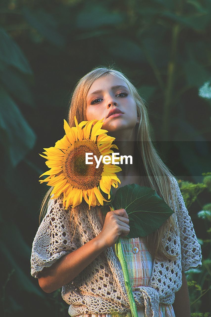 Close-up portrait of teenage girl holding sunflower while standing against plants