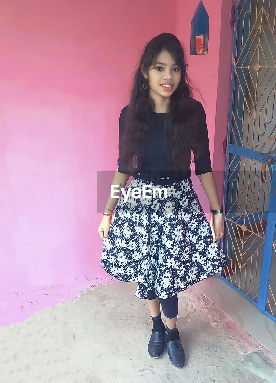 one person, full length, portrait, women, pink, fashion, looking at camera, dress, long hair, hairstyle, standing, clothing, young adult, pattern, adult, front view, photo shoot, smiling, spring, brown hair, happiness, footwear, architecture, purple, indoors, shoe, lifestyles, casual clothing, emotion, person, skirt, child, wall - building feature, arts culture and entertainment, female