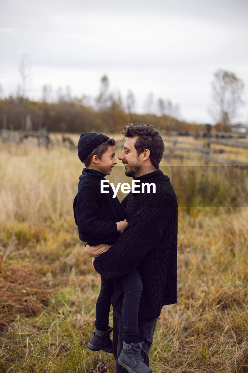 Father and son are standing on a field in autumn in black clothes