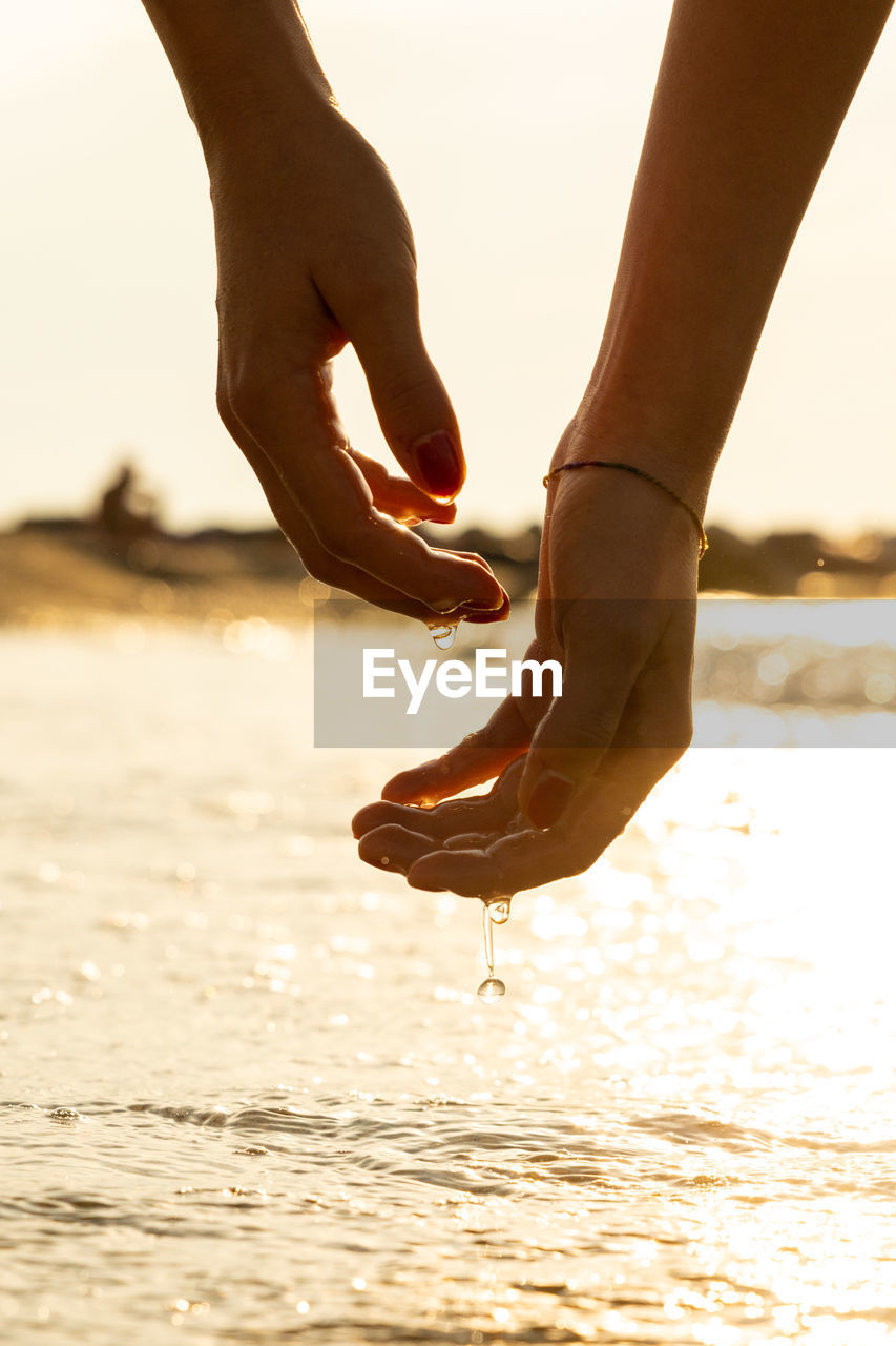 Close-up of hand on sea shore during sunset