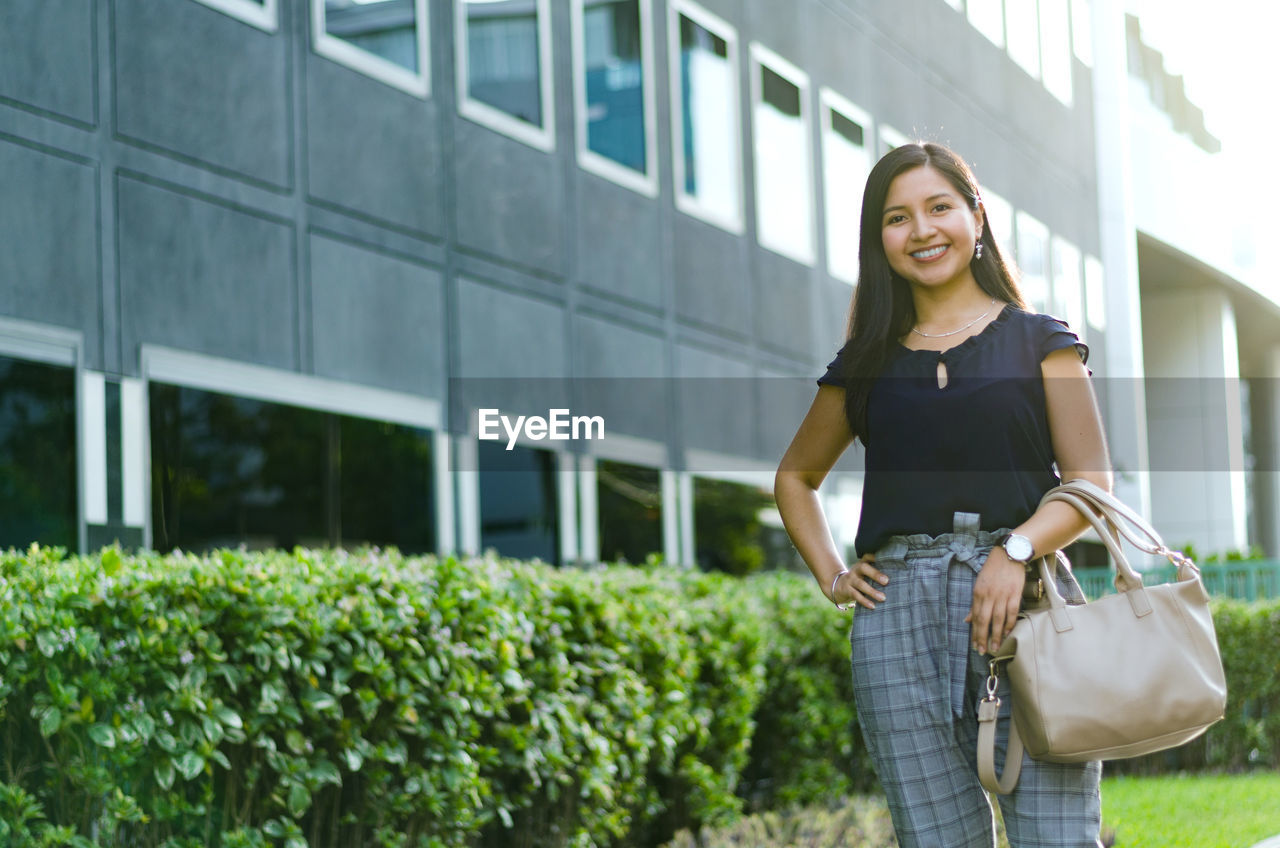 YOUNG WOMAN SMILING WHILE STANDING OUTDOORS