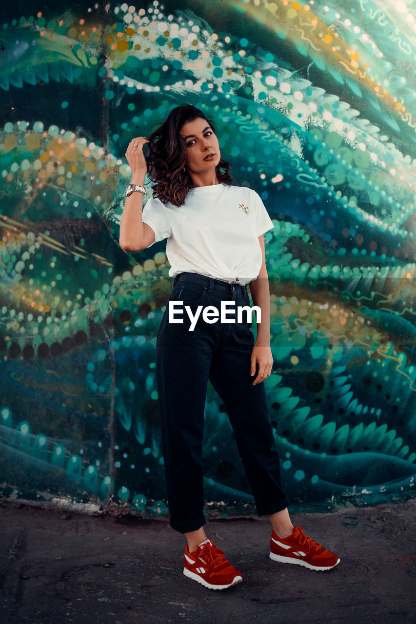 PORTRAIT OF A BEAUTIFUL YOUNG WOMAN STANDING AGAINST WALL