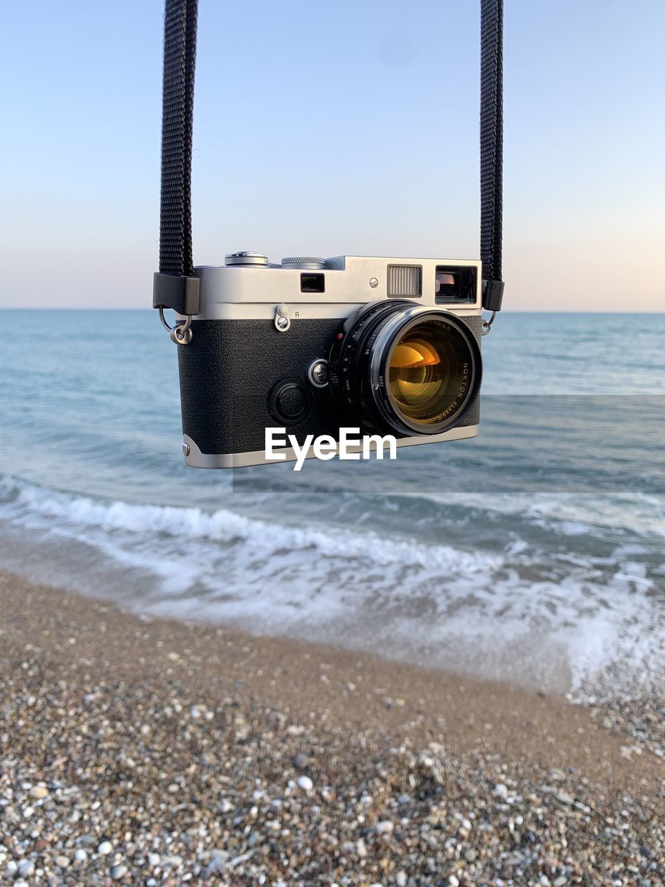 CLOSE-UP OF CAMERA ON BEACH AGAINST THE SKY