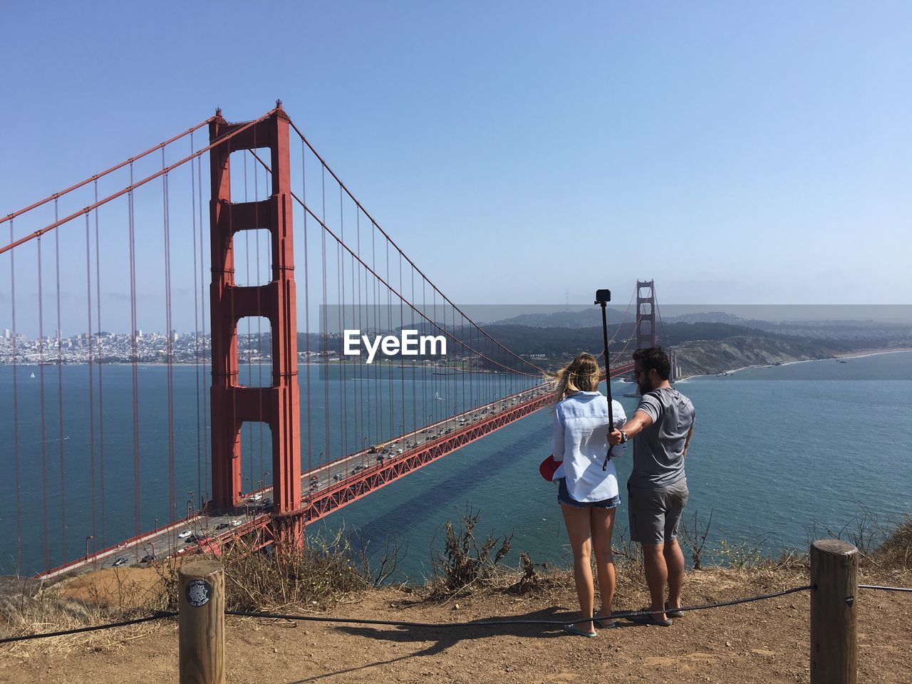 REAR VIEW OF PEOPLE STANDING ON SUSPENSION BRIDGE