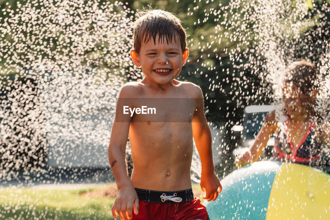 Water splashing on shirtless boy running in yard