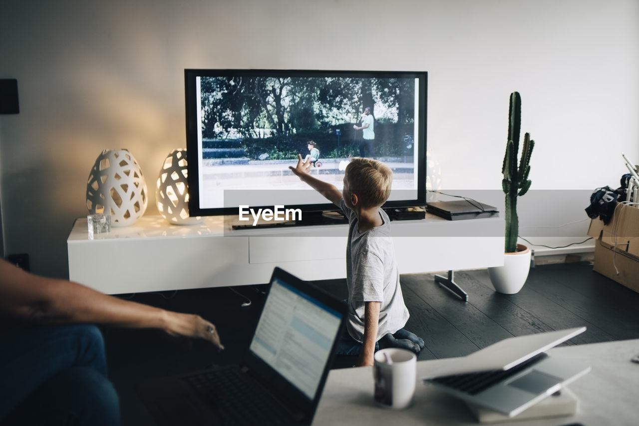 Full length of boy kneeling while touching smart tv in living room at home