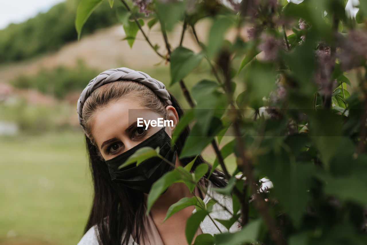 Woman with face mask looking behind the tree in nature