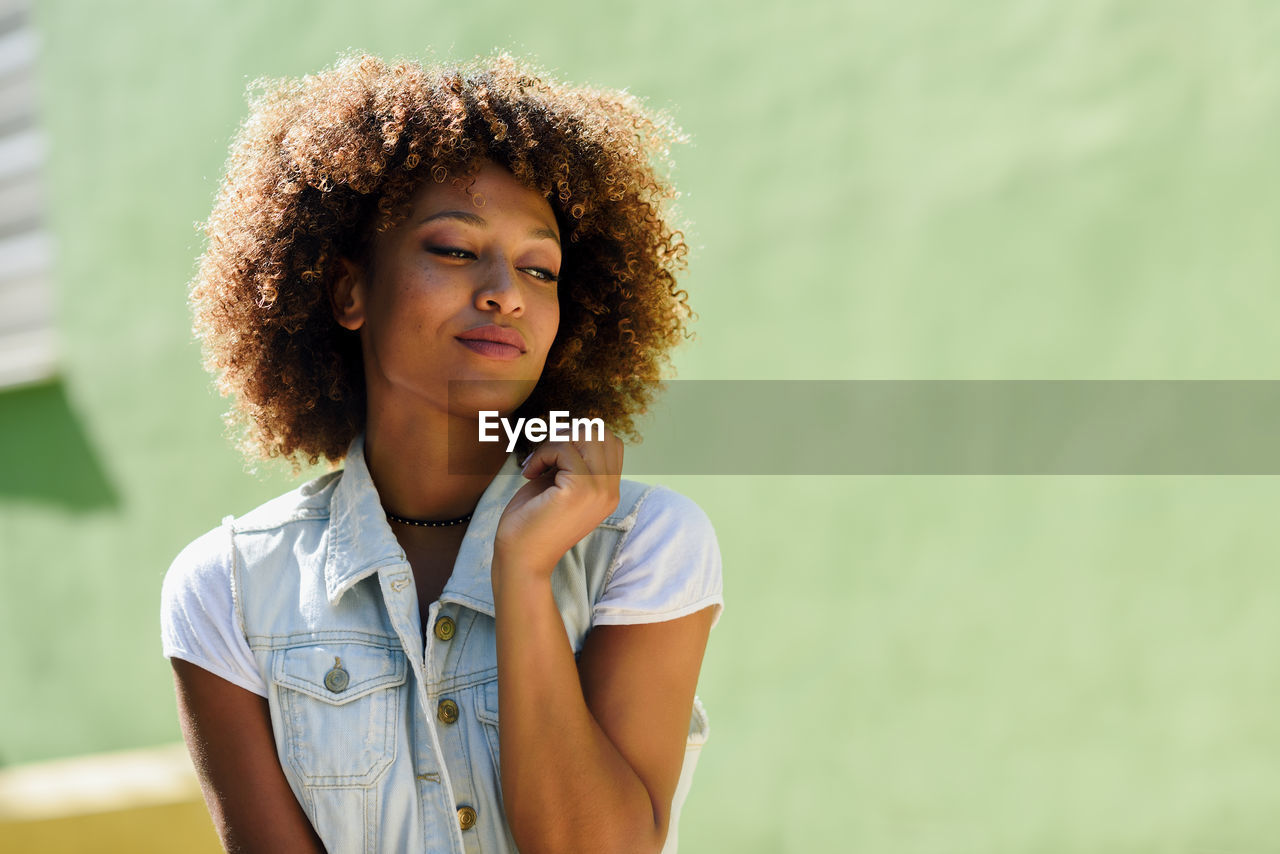 Close-up of young woman with curly hair against green wall