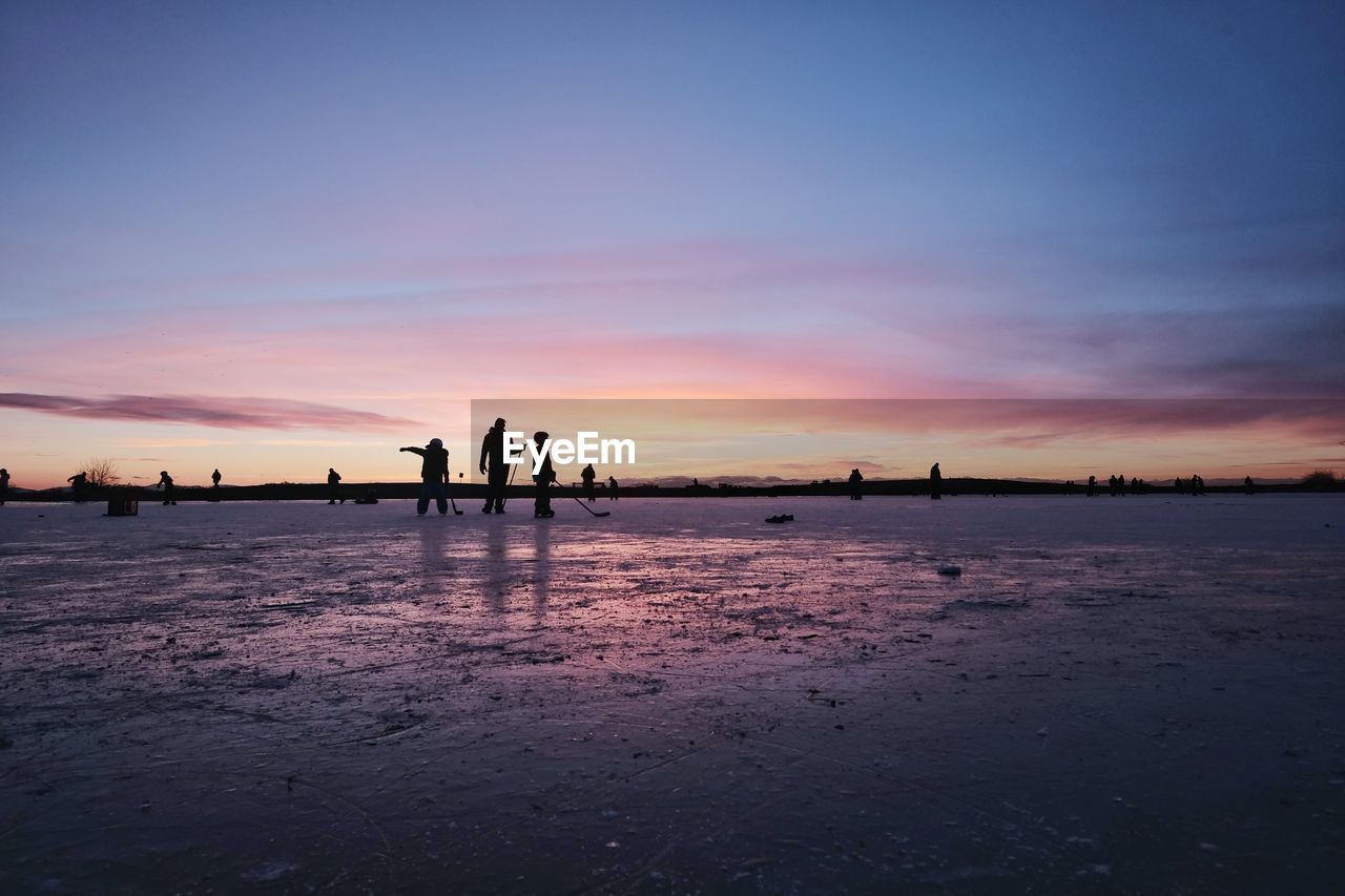 Silhouette people on ice against sky during sunset