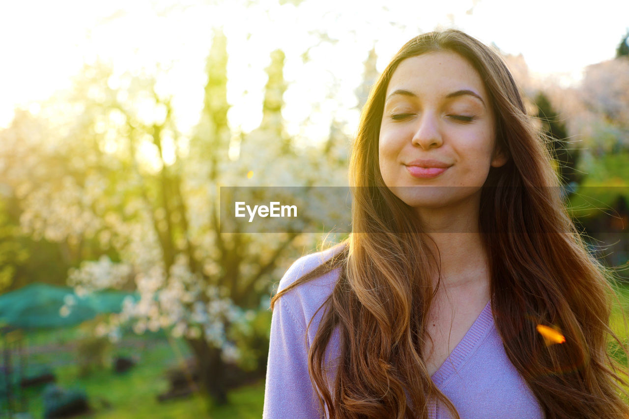 Beautiful young woman with eyes closed against trees