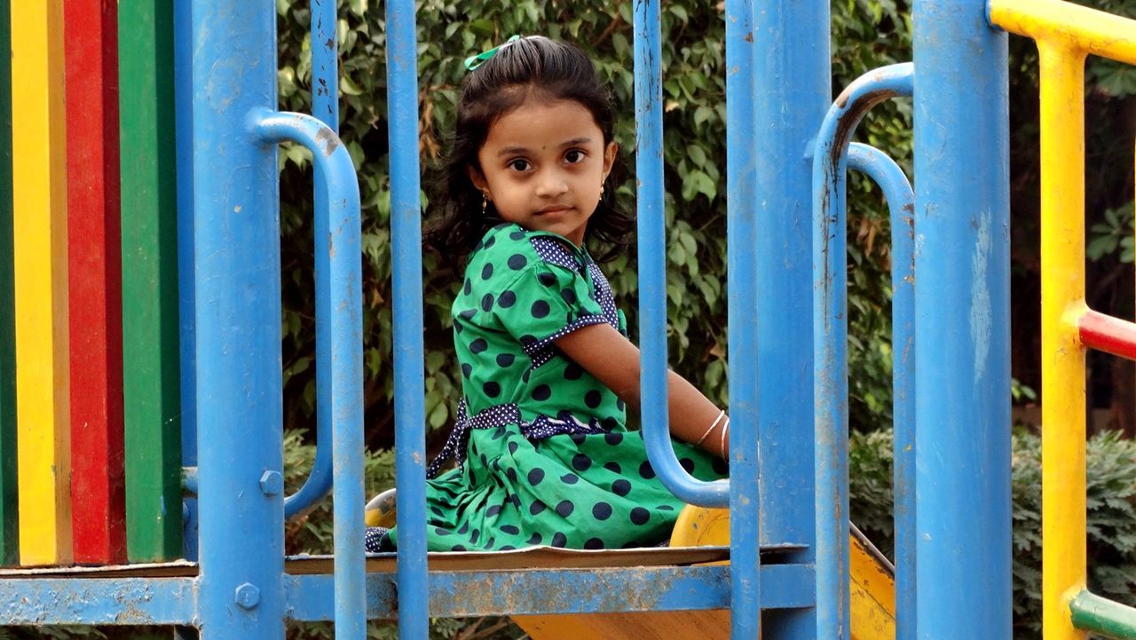 Portrait of girl sitting on colorful play equipment at park