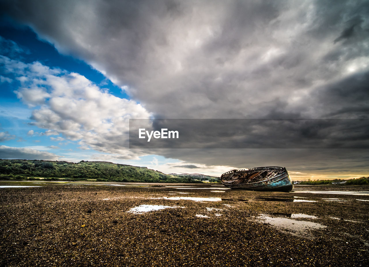 Abandoned boat at shore against cloudy sky