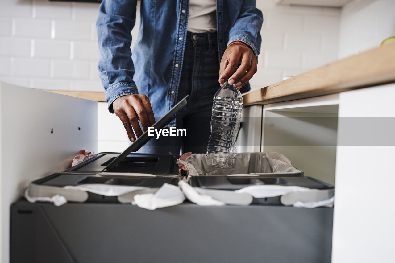 Young woman recycling plastic bottles in kitchen at home