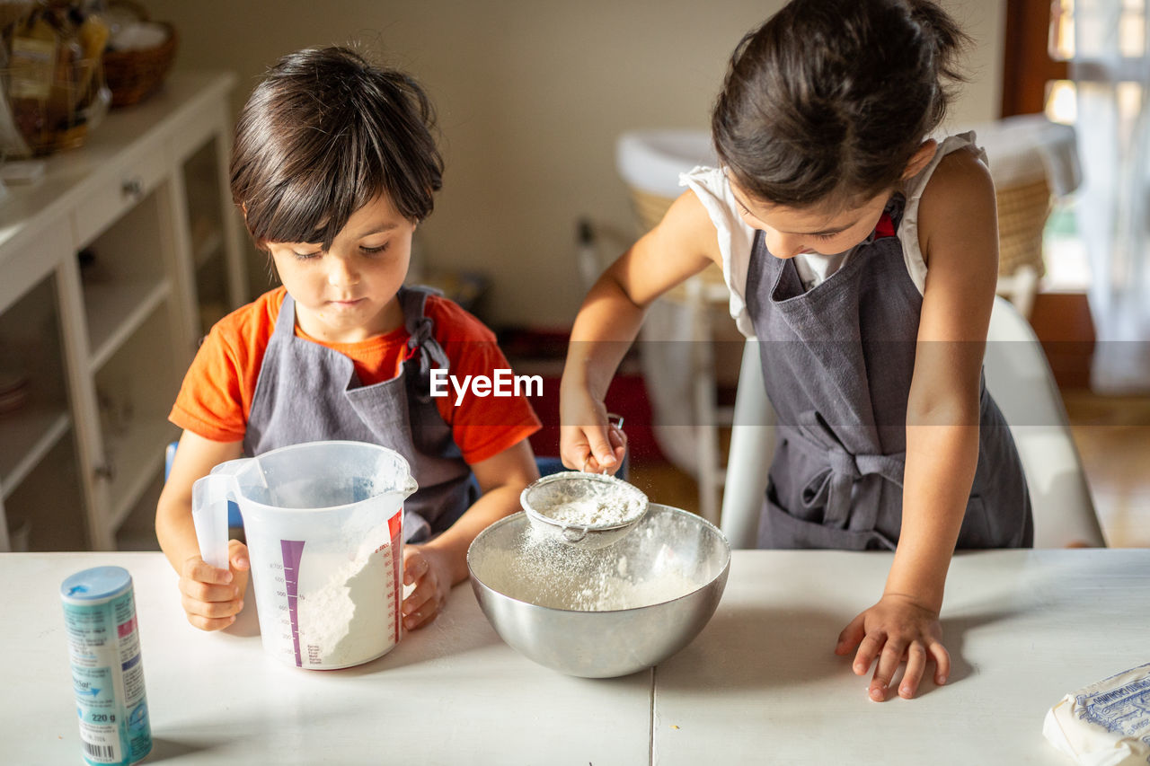 Two girls wearing grey aprons sifting flour