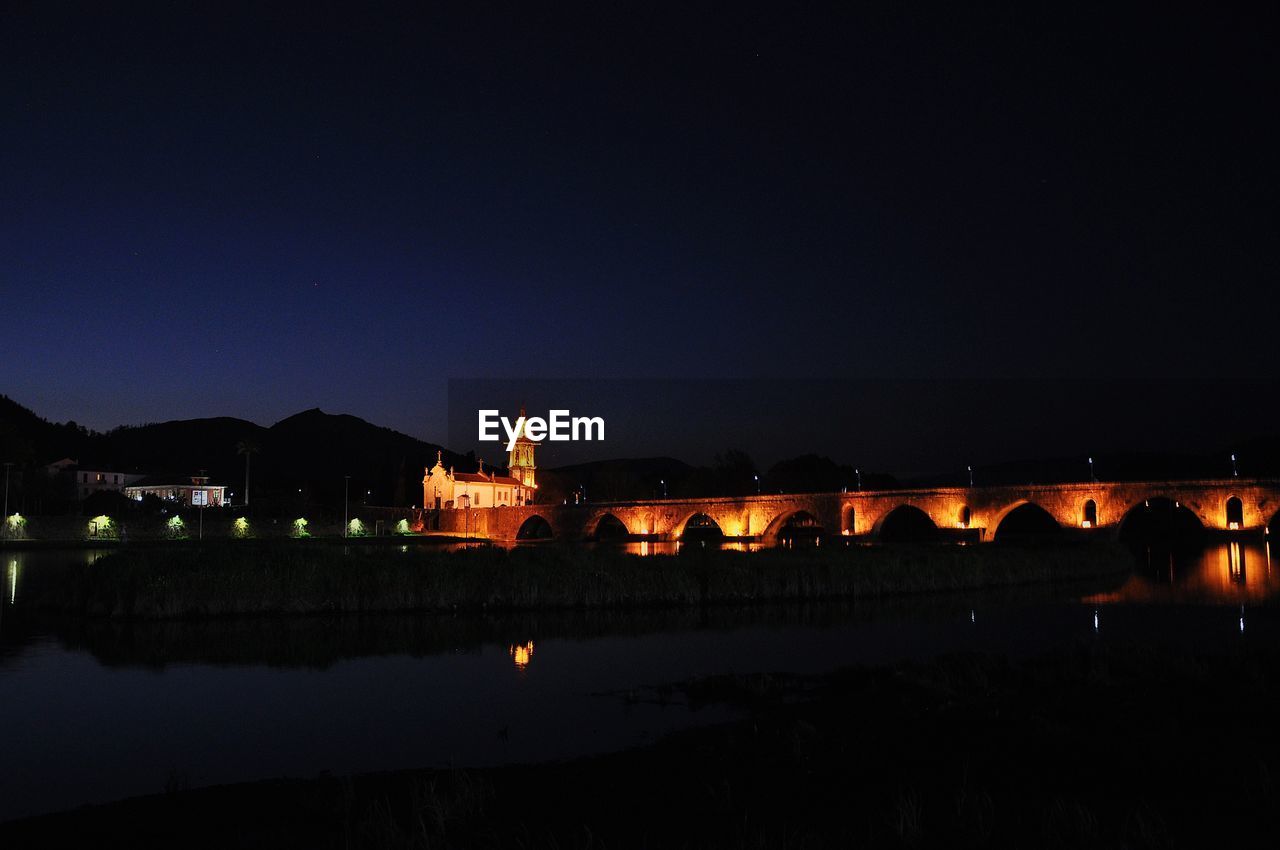 ILLUMINATED BUILDINGS BY RIVER AGAINST SKY