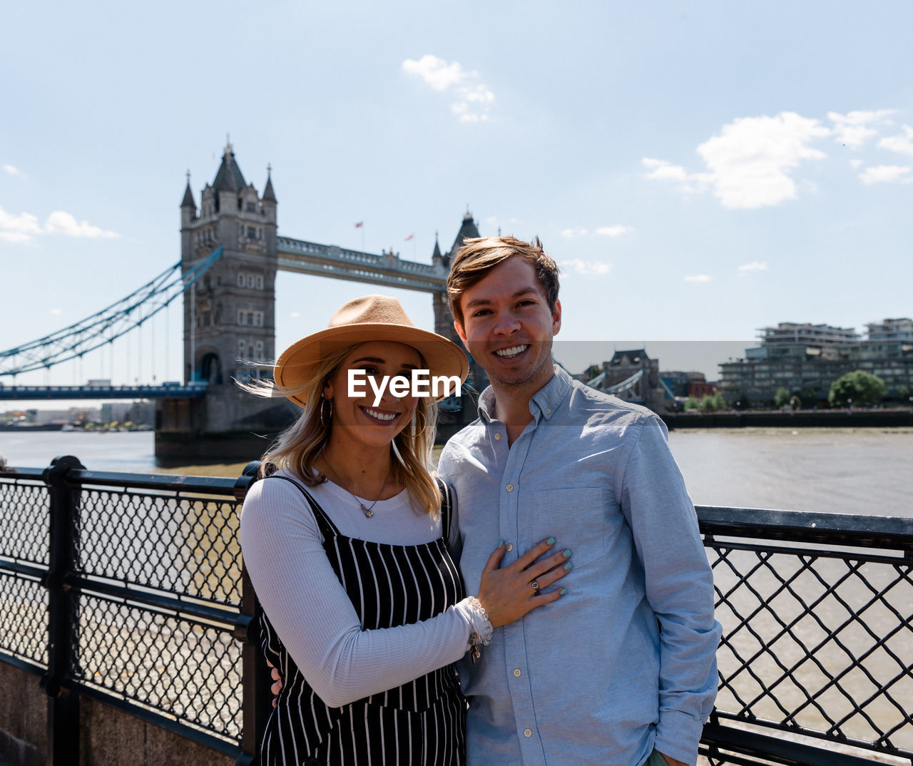 Portrait of young couple standing against tower bridge and sky
