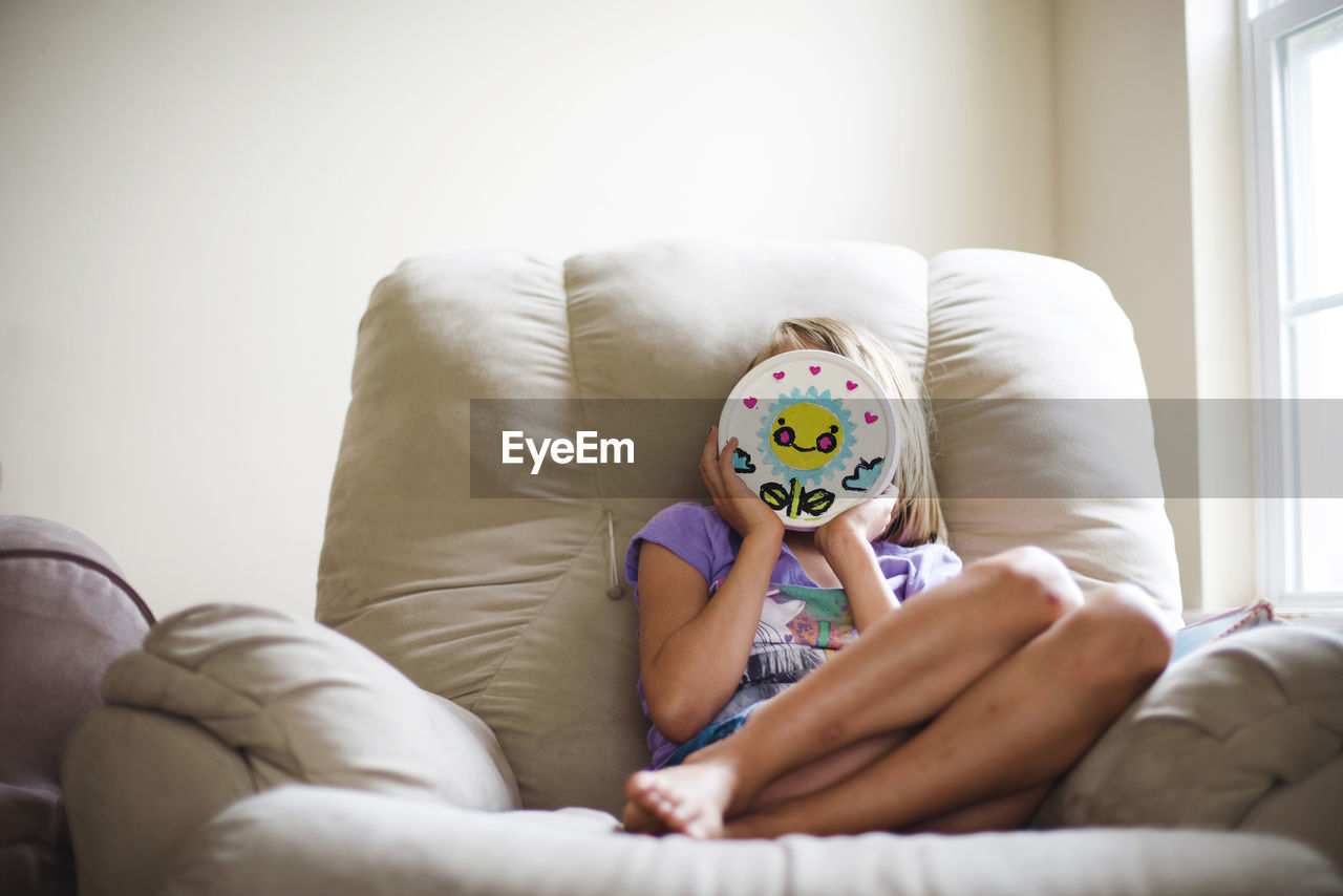Girl holding toy against her face while sitting on couch against wall