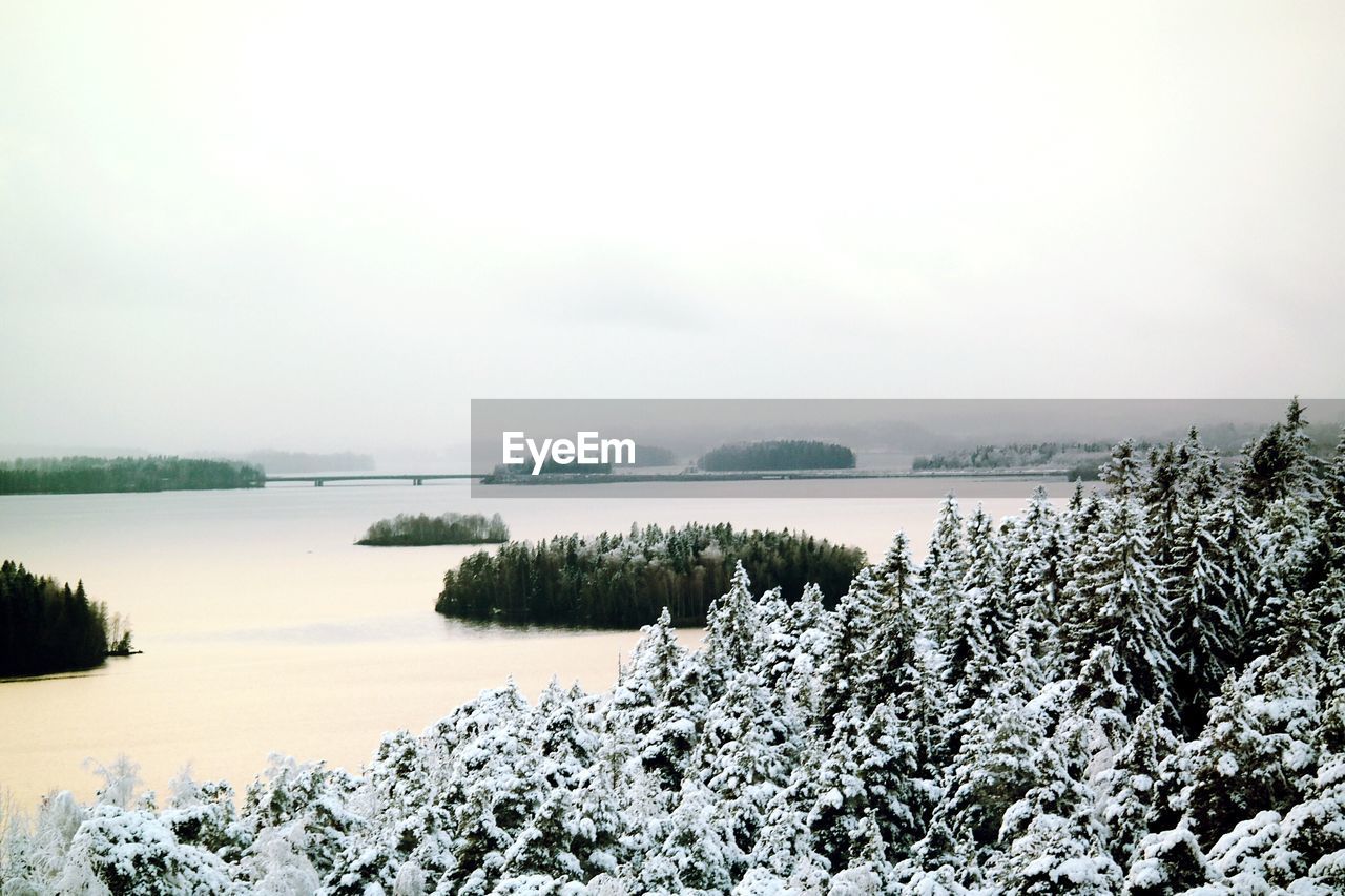 Scenic view of snow-covered trees by sea against sky