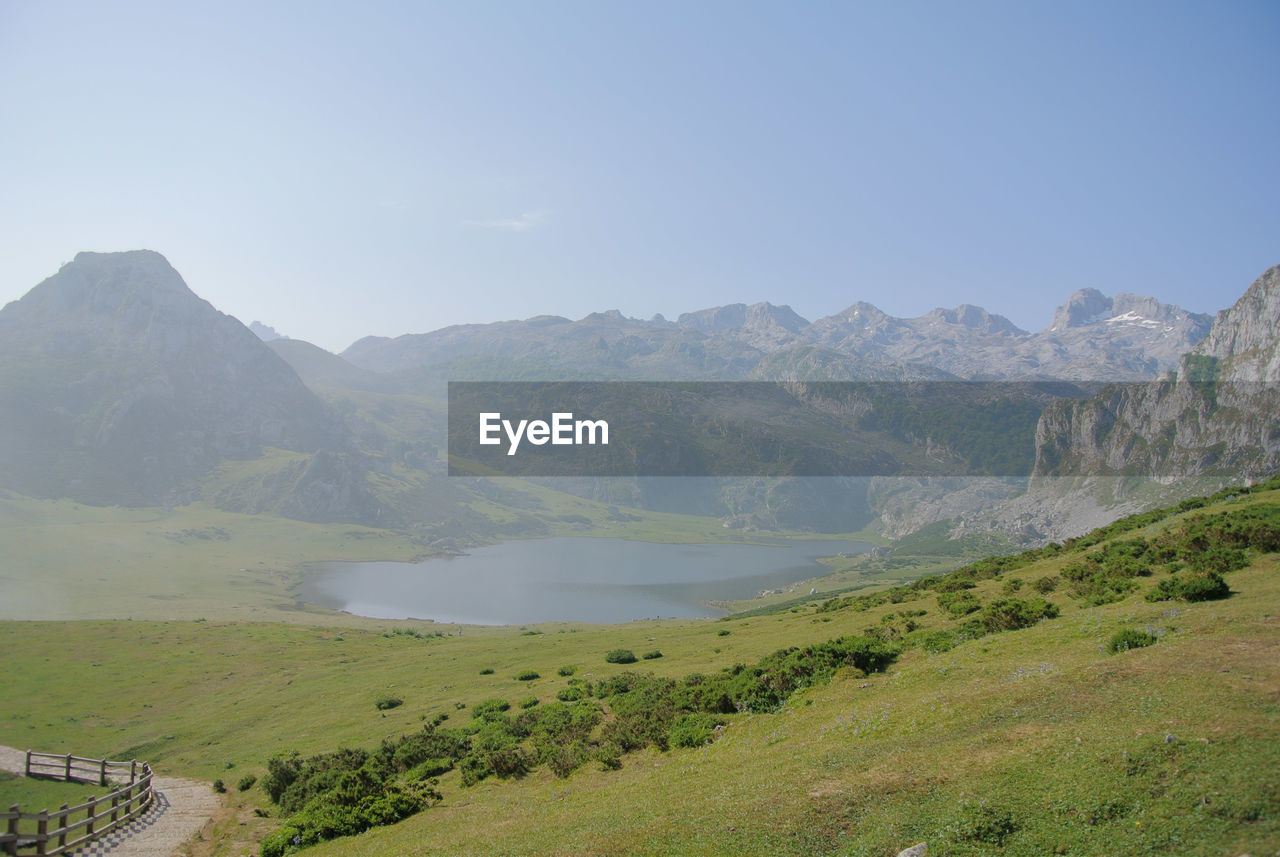 mountain, environment, scenics - nature, landscape, beauty in nature, sky, nature, mountain range, land, lake, highland, water, plant, travel, mountain pass, tranquility, travel destinations, valley, no people, tranquil scene, grass, day, tourism, ridge, outdoors, non-urban scene, plateau, clear sky, green, tree, blue, reservoir, road, idyllic, rural scene, sunny, activity, vacation