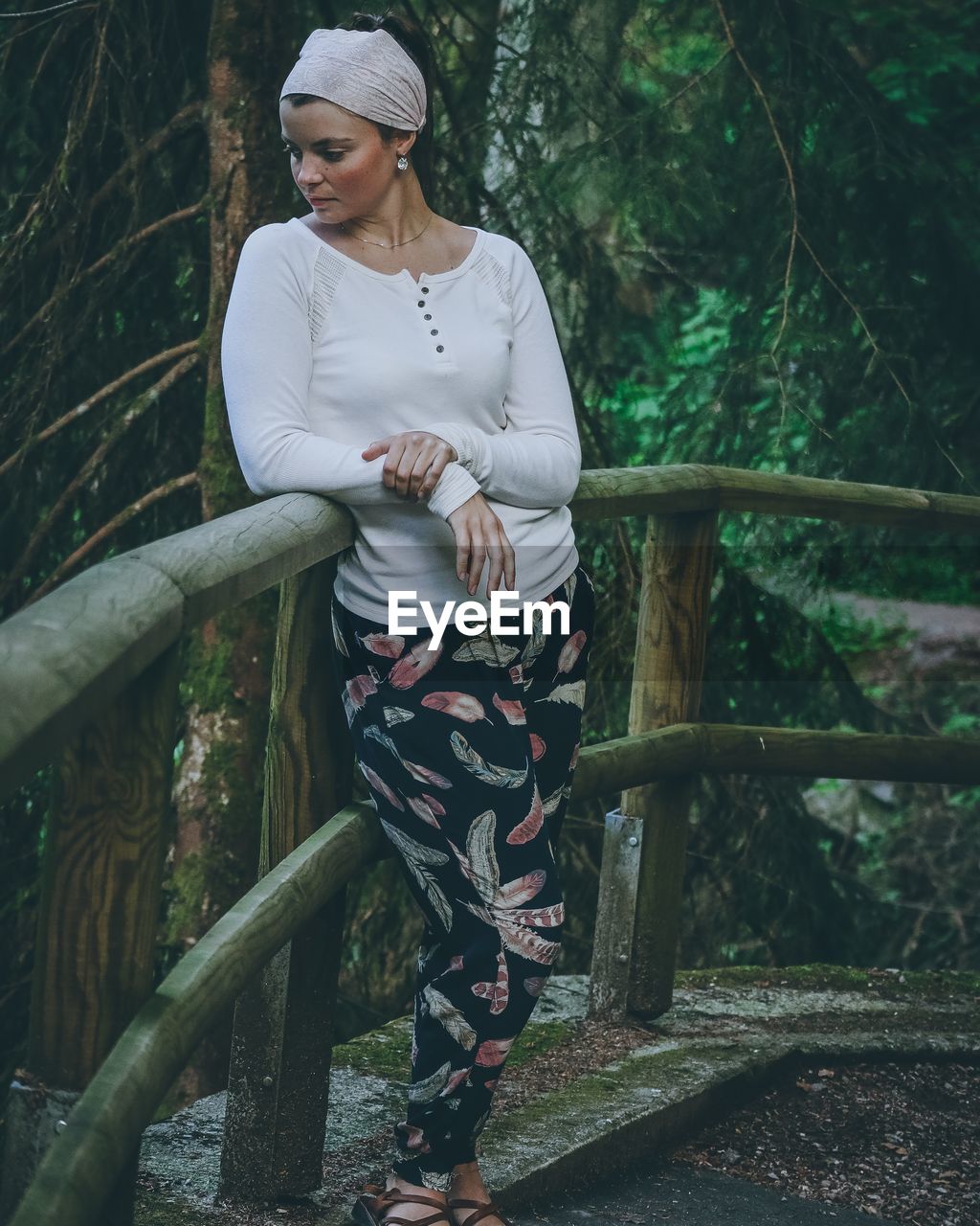 Full length of woman standing by railing against trees in forest
