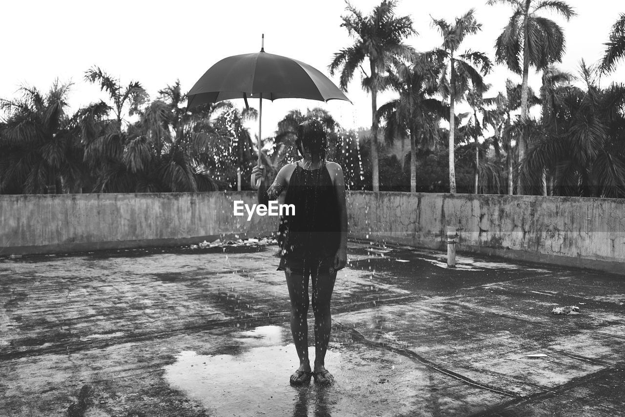 Full length of woman holding umbrella during rainy season at building terrace