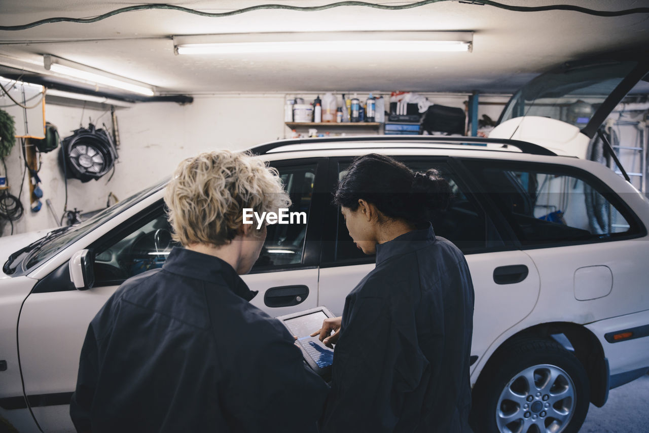 Female mechanic explaining coworker over digital tablet in auto repair shop