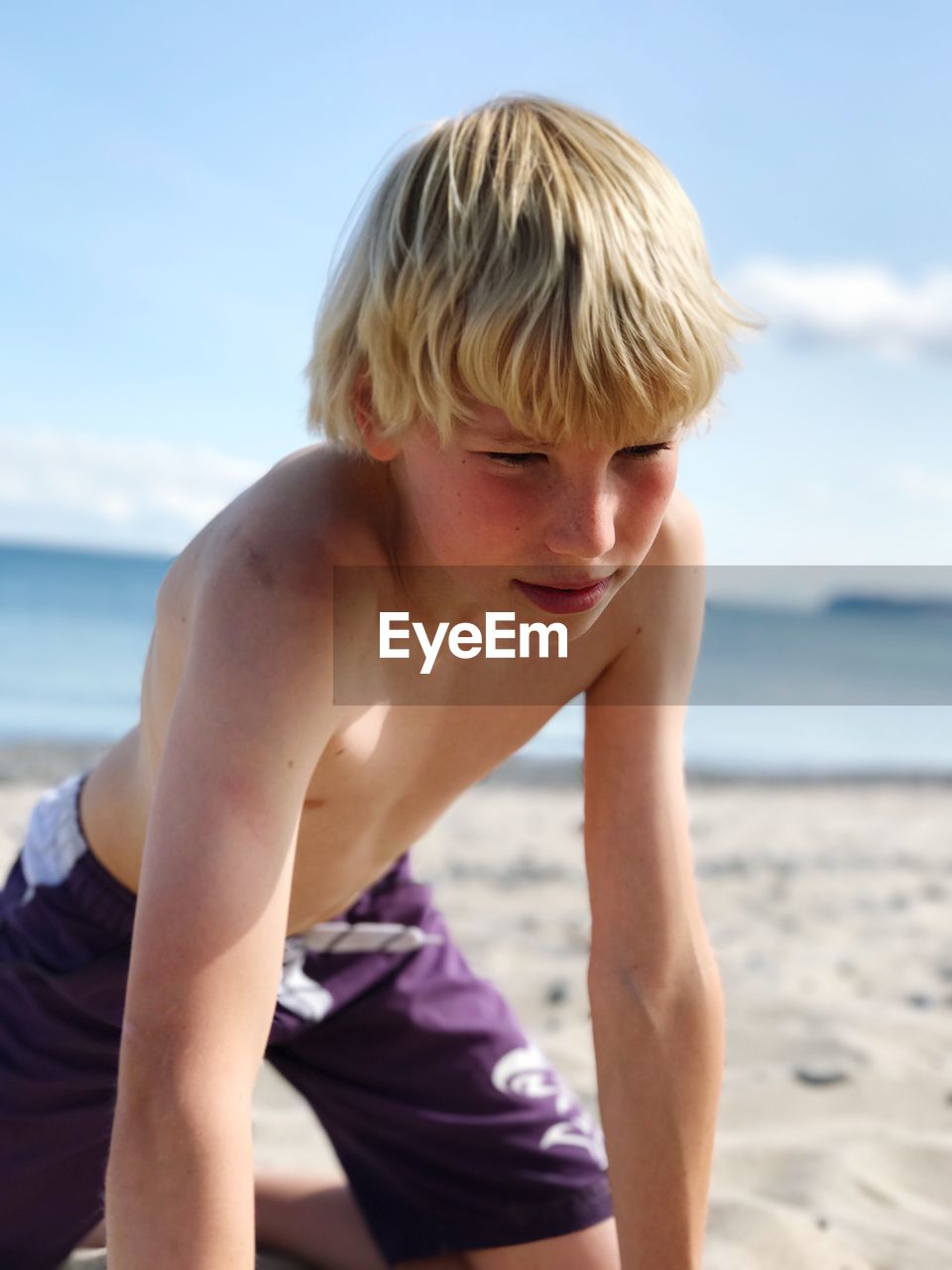 Shirtless teenage boy kneeling at beach