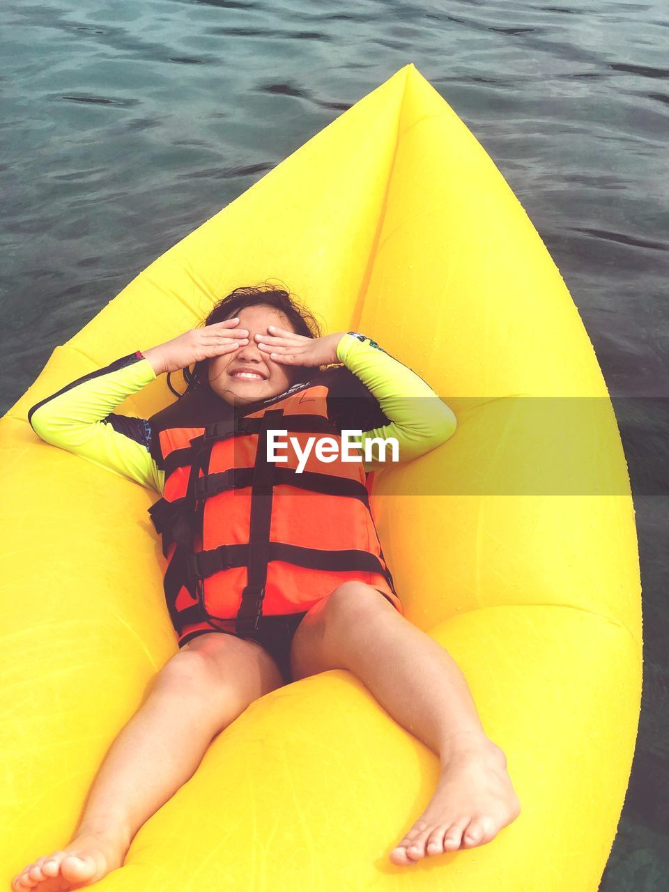 High angle view of girl wearing life jacket lying on yellow raft at sea