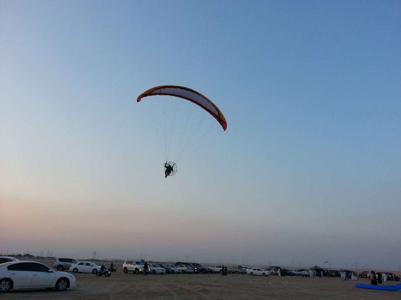 Man powered paragliding over landscape against sky during sunset