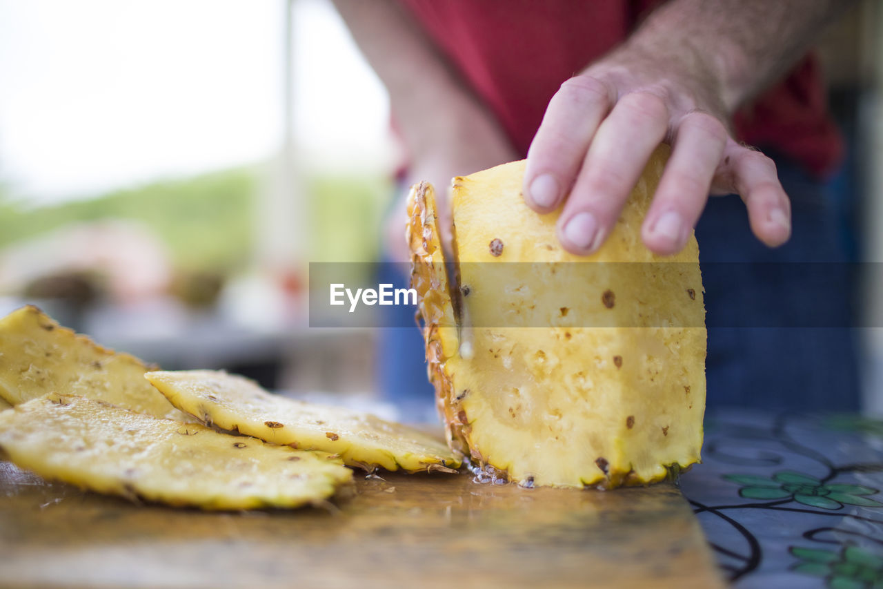 Detailed view of man slicing fresh pineapple outdoors