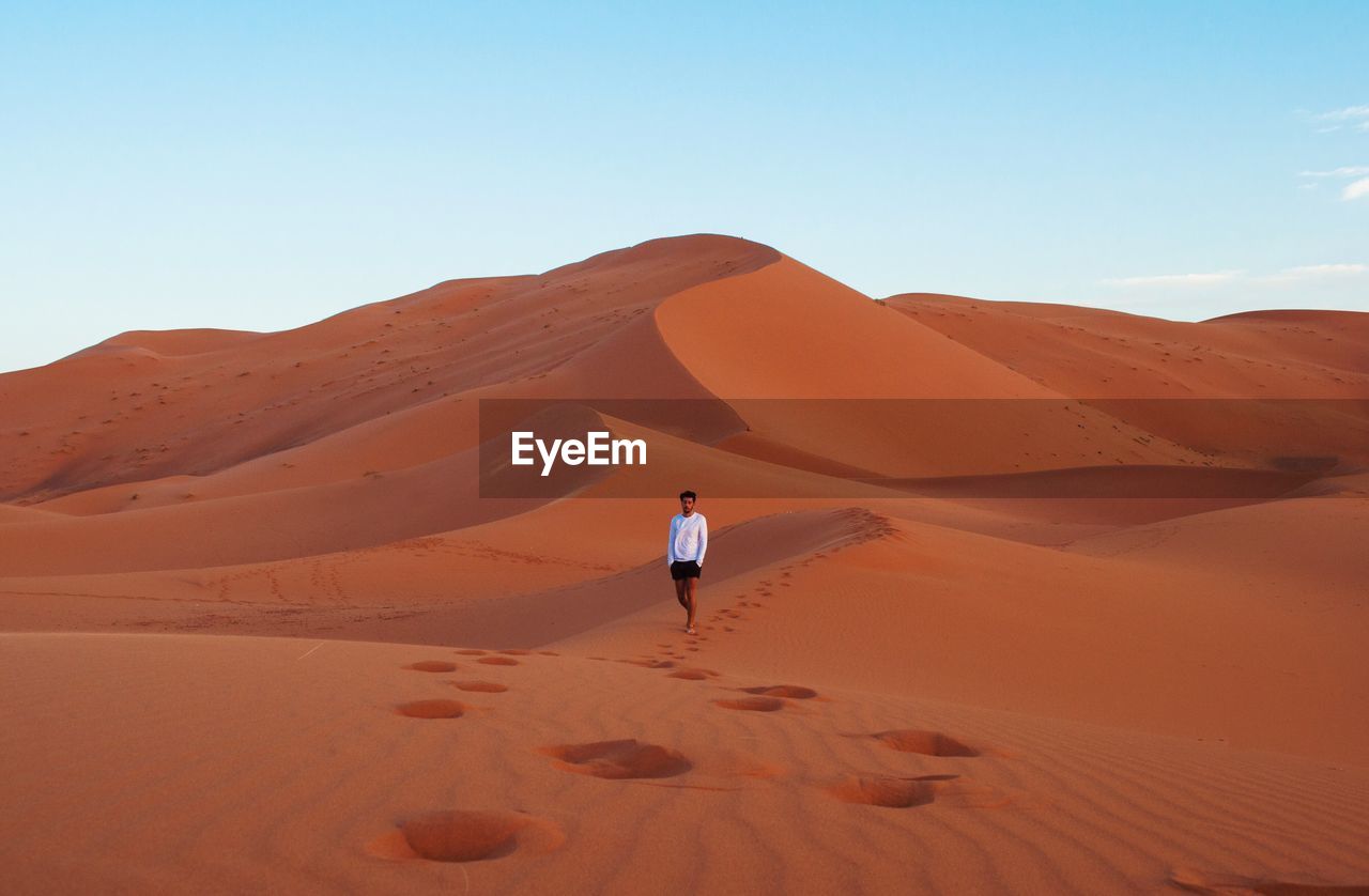 Man walking on sand dune at sahara desert against sky