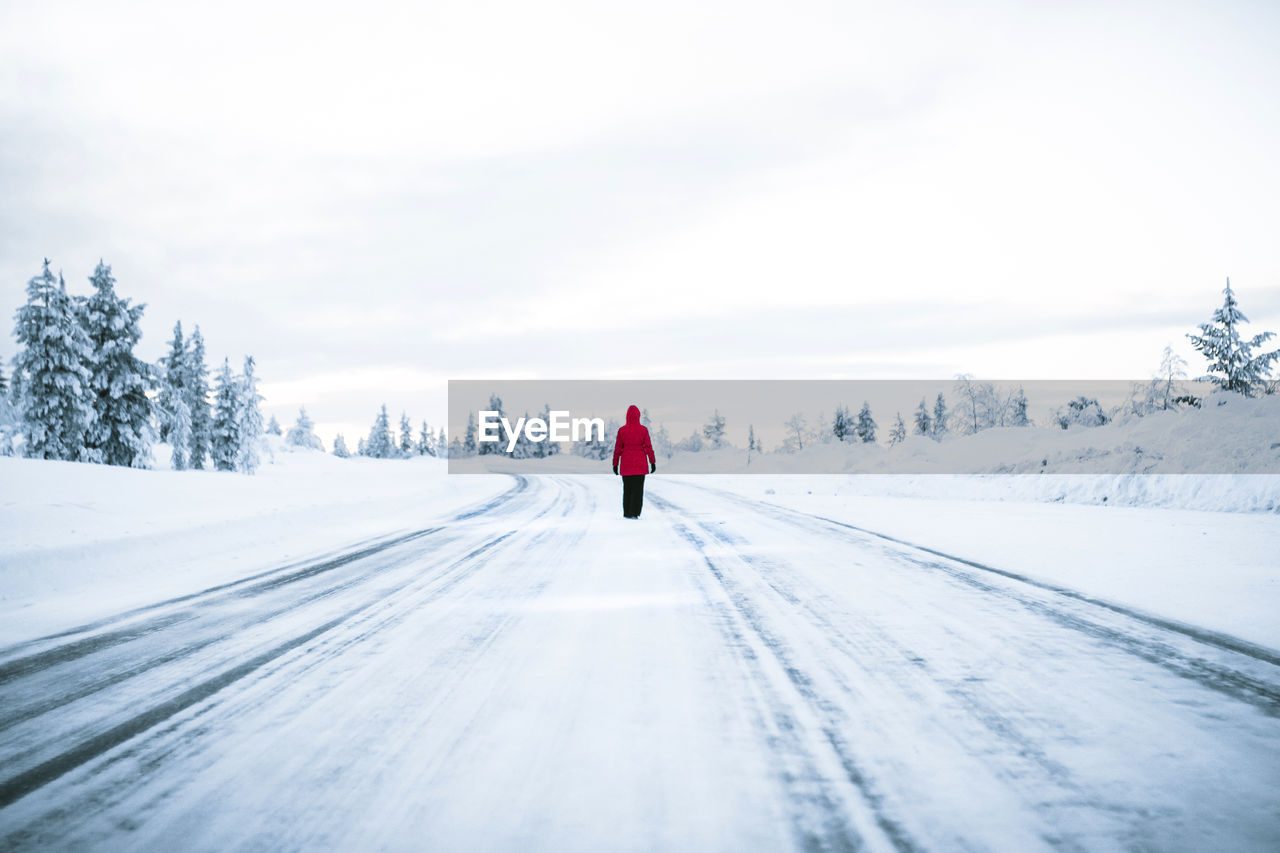 Rear view of person walking on snow covered street against sky